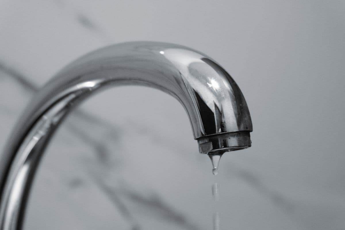 A chrome bathroom faucet with a slow drip forming at the spout
